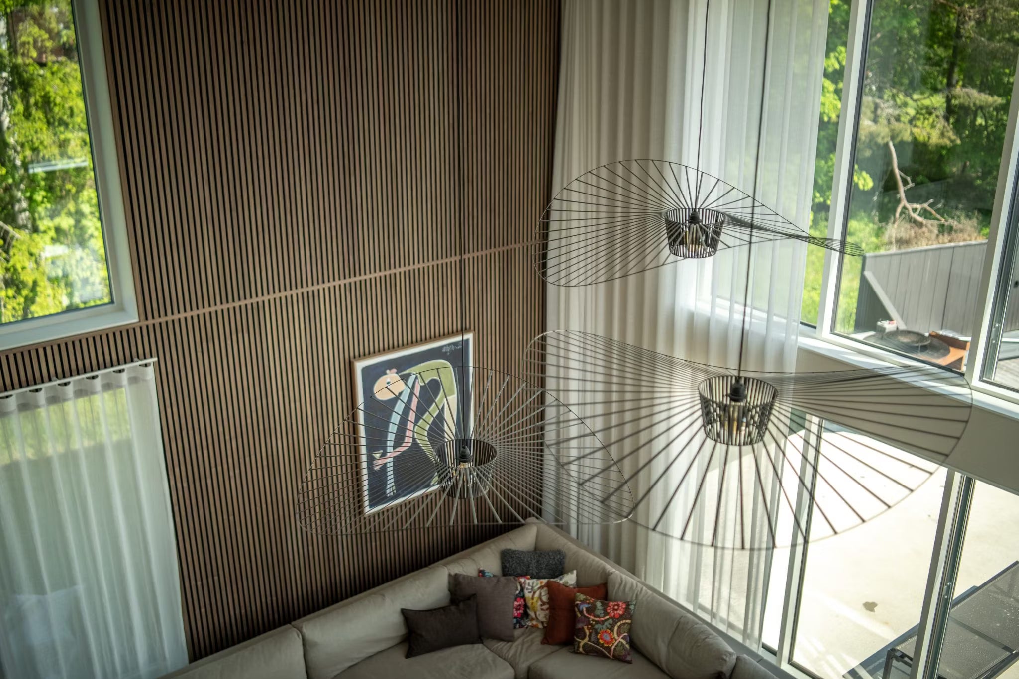 Soggiorno moderno con pareti in legno nordico Akupanel, grandi finestre, pannelli acustici astratti, un divano componibile e apparecchi di illuminazione minimalisti, visti dallalto.